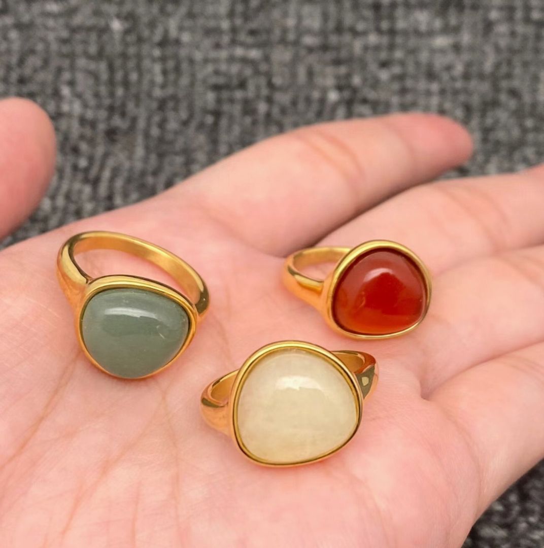 Three gold rings with different colored stones on a hand against a textured gray background