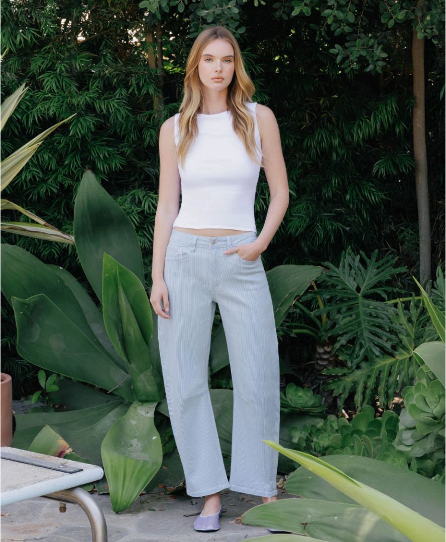 Woman wearing a white sleeveless top and light blue jeans standing in a garden.