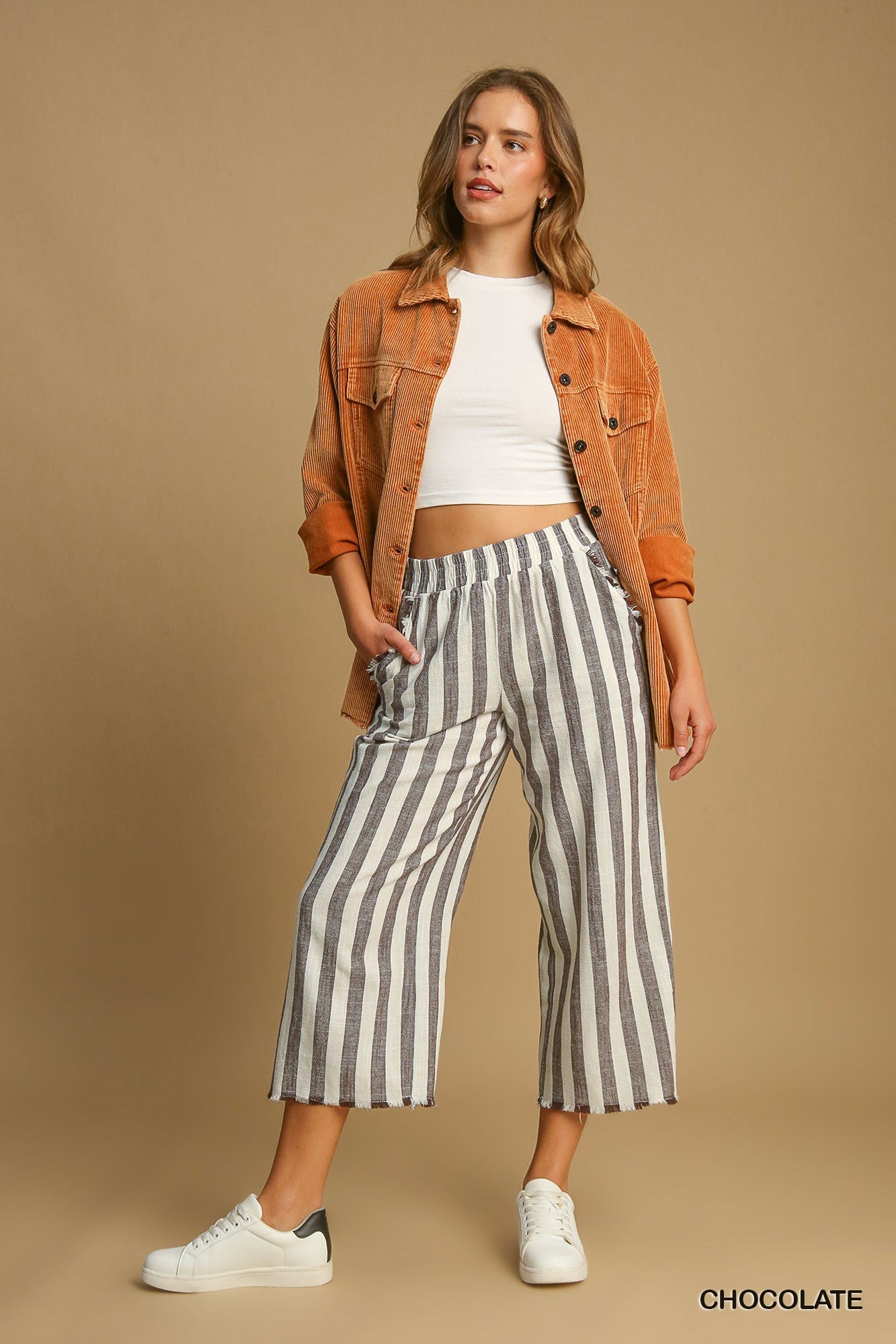 Woman wearing a brown jacket, white top, and striped pants on a beige background