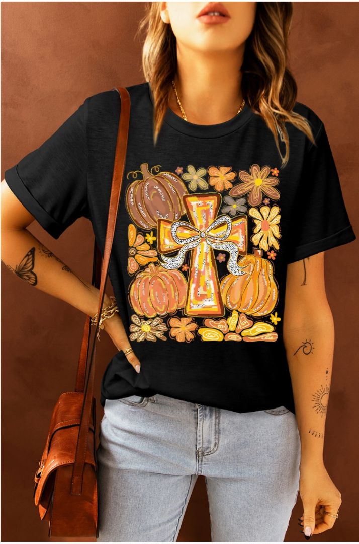 Person wearing a black t-shirt with a colorful graphic design featuring pumpkins and a cross, standing against a brown background.