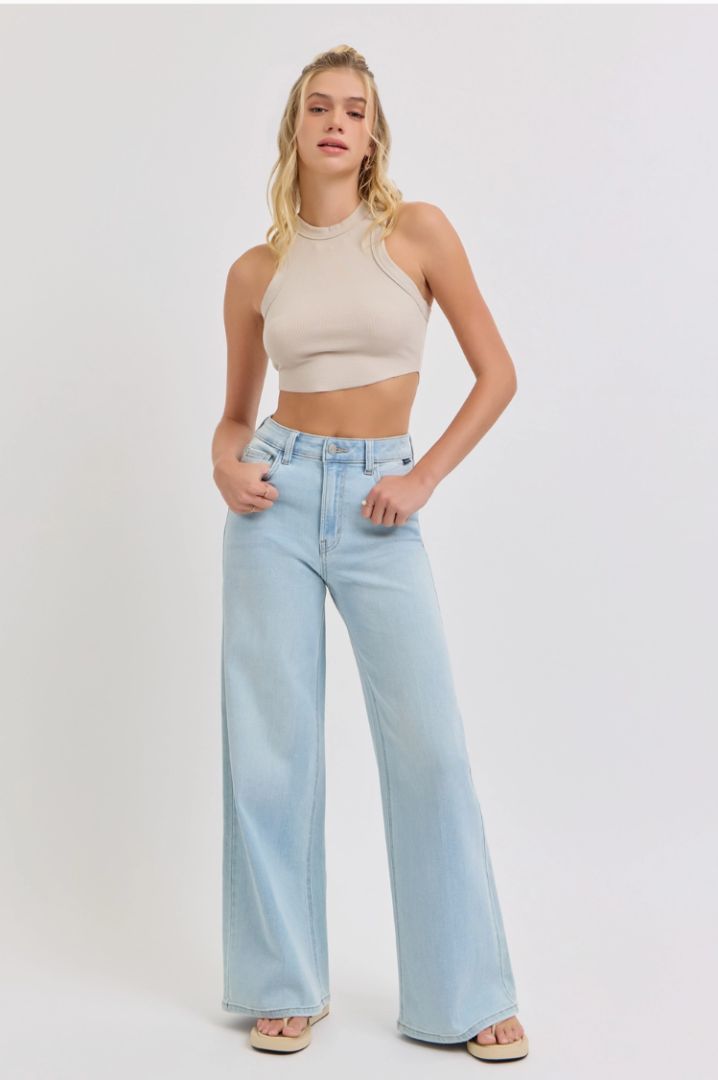 Woman wearing a beige crop top and light blue jeans on a white background